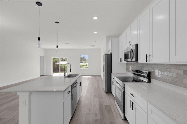 kitchen featuring stainless steel appliances, a sink, light wood-type flooring, backsplash, and an island with sink