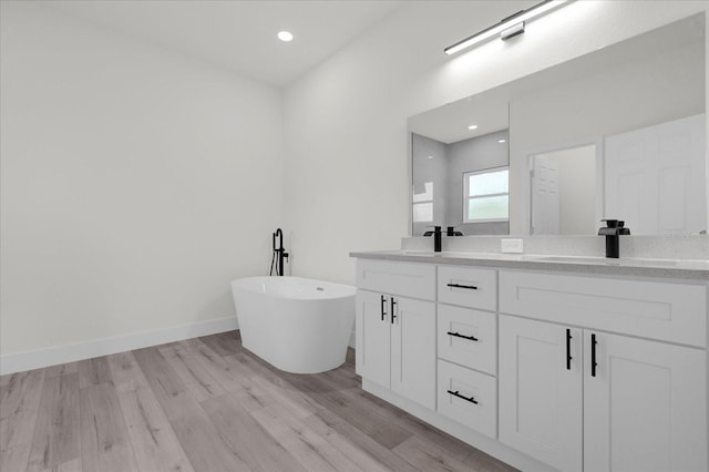 full bath with double vanity, a freestanding bath, a sink, wood finished floors, and baseboards