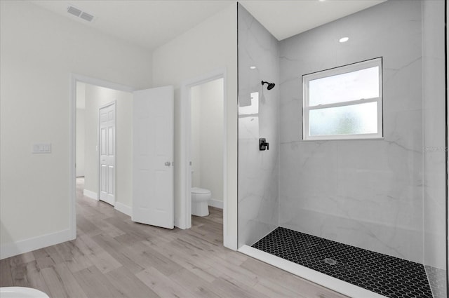 bathroom featuring toilet, hardwood / wood-style flooring, and a tile shower