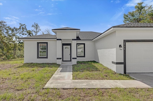 prairie-style house with a front lawn, a shingled roof, an attached garage, and stucco siding