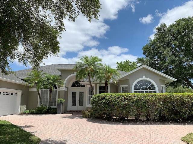 14421 Hatchee Ct, Orlando, FL 32837 - view of front of home featuring a shingled roof, a garage, stucco siding, decorative driveway, and french doors