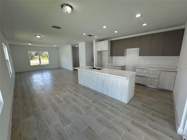 kitchen with light wood-type flooring, a textured ceiling, a kitchen island with sink, and sink