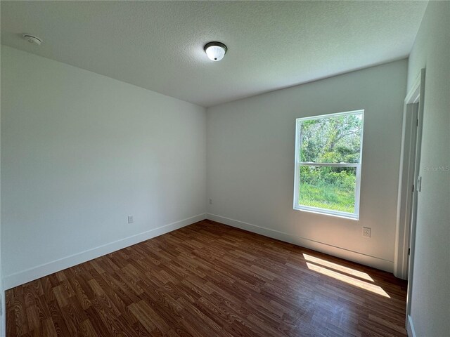 spare room with a textured ceiling and dark hardwood / wood-style flooring