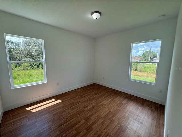 unfurnished room with dark wood-style floors, a healthy amount of sunlight, and baseboards