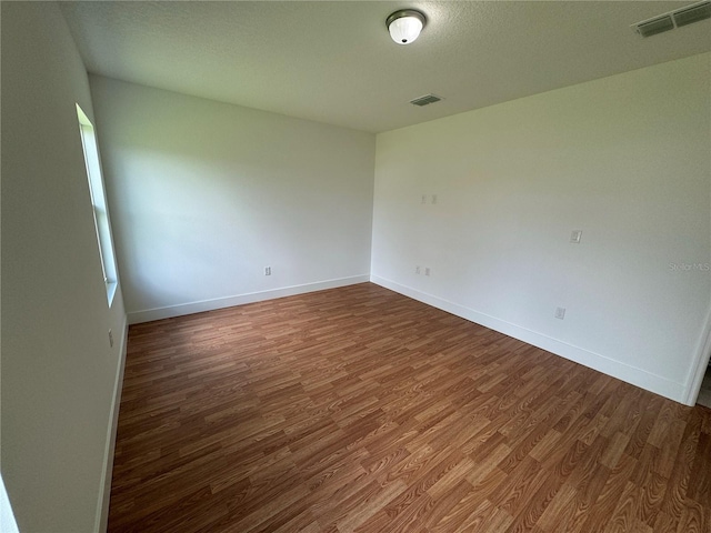empty room with wood finished floors, visible vents, and baseboards