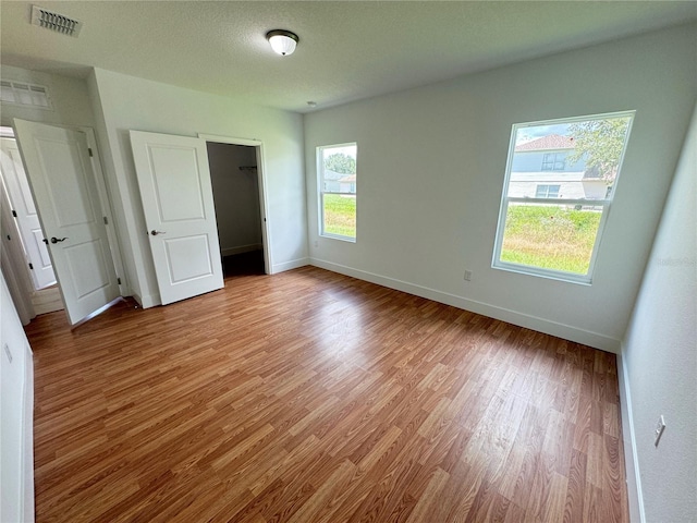 unfurnished bedroom featuring visible vents, a textured ceiling, baseboards, and wood finished floors