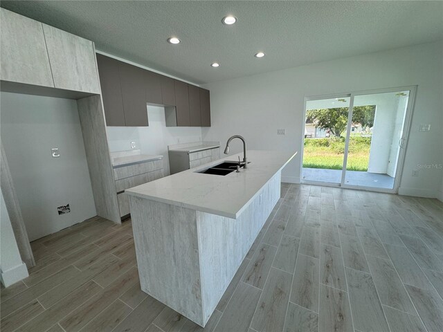 kitchen featuring a textured ceiling, light stone counters, sink, a center island with sink, and light hardwood / wood-style floors