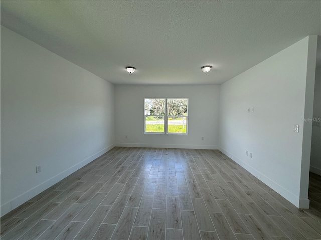 spare room featuring baseboards, a textured ceiling, and wood finished floors
