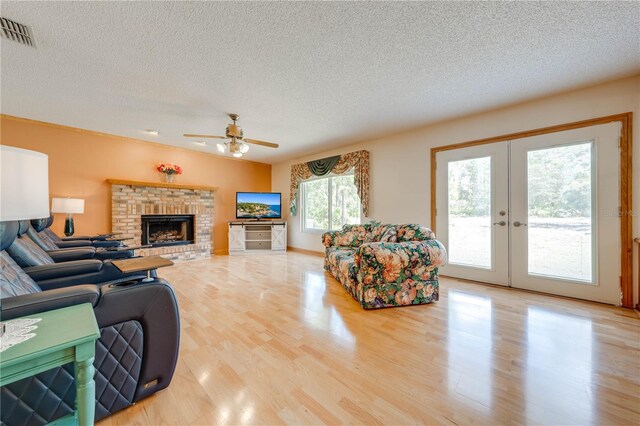 living room featuring ceiling fan, a textured ceiling, light wood-type flooring, and a fireplace