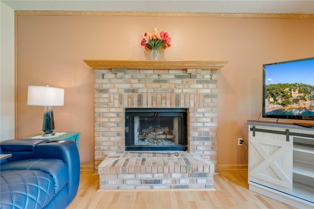 living room with a barn door, a brick fireplace, a textured ceiling, and light hardwood / wood-style floors