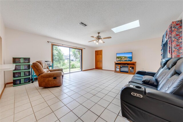 living room with a skylight, ceiling fan, a textured ceiling, and light tile patterned flooring