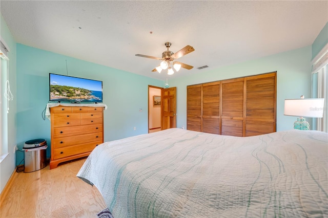 bedroom with a closet, a textured ceiling, light wood-type flooring, and ceiling fan