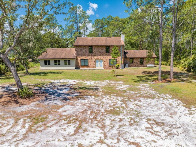 1775 Sundance Dr, Saint Cloud, FL 34771 - view of front facade featuring a chimney, a front lawn, brick siding, central air condition unit, and view of wooded area