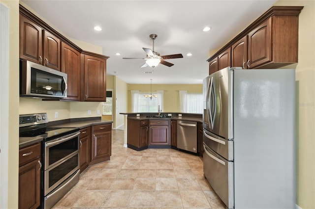 kitchen with hanging light fixtures, ceiling fan with notable chandelier, stainless steel appliances, dark brown cabinetry, and sink