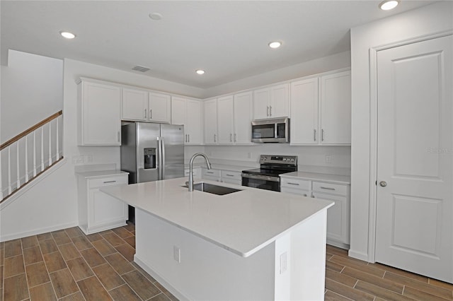 kitchen with appliances with stainless steel finishes, sink, white cabinetry, and an island with sink