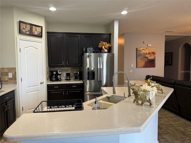 kitchen with dark tile patterned flooring, a kitchen island with sink, stainless steel fridge with ice dispenser, sink, and backsplash