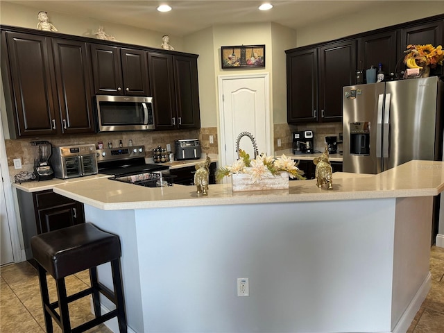 kitchen with a kitchen island with sink, appliances with stainless steel finishes, tasteful backsplash, and a breakfast bar area