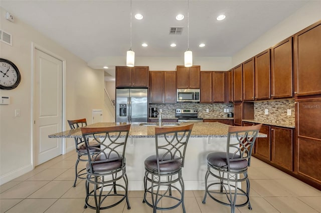 kitchen with hanging light fixtures, stainless steel appliances, sink, a center island with sink, and a breakfast bar