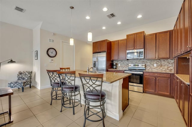 kitchen featuring a kitchen island with sink, appliances with stainless steel finishes, decorative light fixtures, and light stone countertops