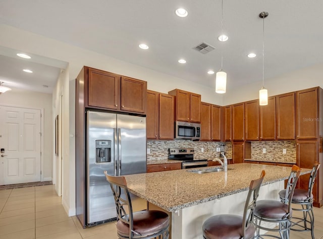 kitchen featuring hanging light fixtures, stainless steel appliances, a kitchen breakfast bar, decorative backsplash, and a center island with sink