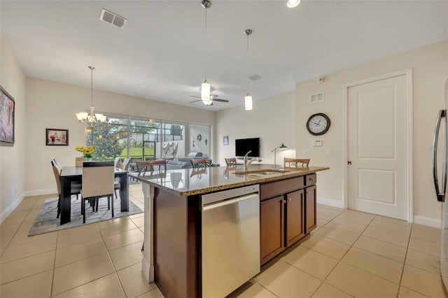 kitchen with ceiling fan with notable chandelier, appliances with stainless steel finishes, an island with sink, sink, and light stone counters