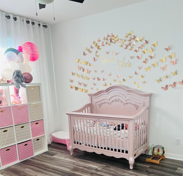 bedroom with hardwood / wood-style floors, ceiling fan, and a nursery area