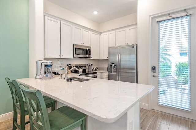 kitchen featuring plenty of natural light, stainless steel appliances, kitchen peninsula, and white cabinetry