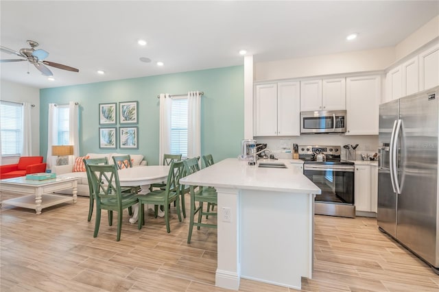 kitchen featuring light wood-type flooring, stainless steel appliances, white cabinetry, kitchen peninsula, and ceiling fan