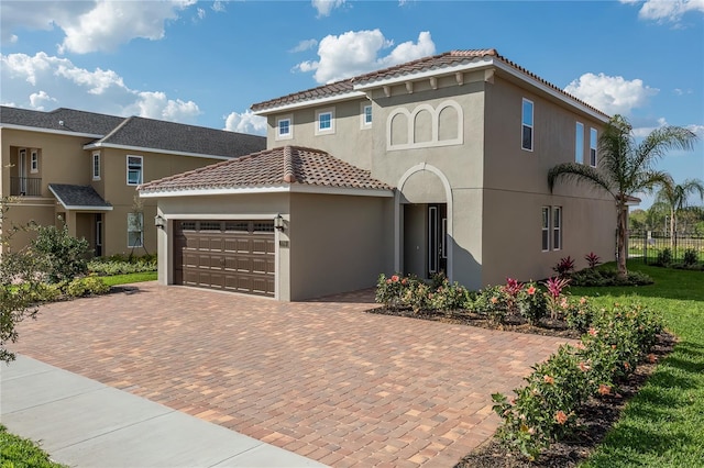 mediterranean / spanish home featuring stucco siding, an attached garage, a tile roof, and decorative driveway