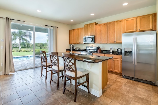 kitchen featuring a kitchen breakfast bar, a center island with sink, stainless steel appliances, sink, and dark stone countertops