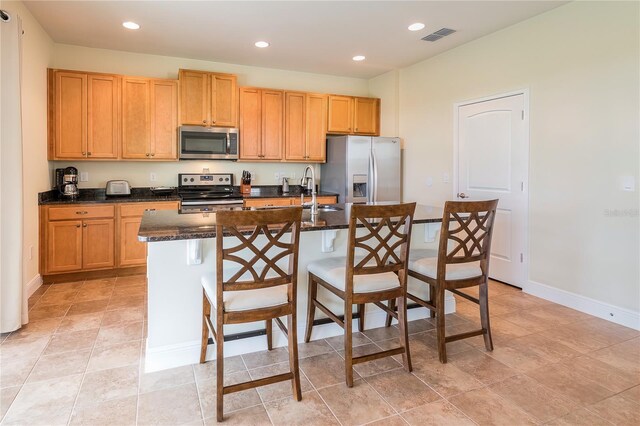 kitchen with appliances with stainless steel finishes, an island with sink, a breakfast bar, sink, and dark stone countertops