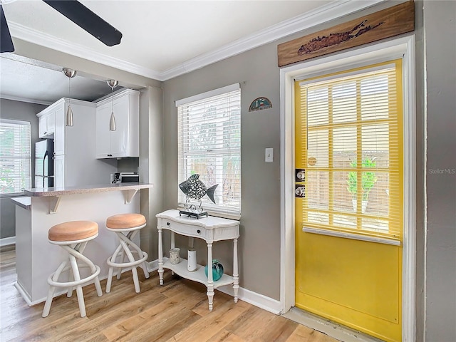 kitchen featuring light hardwood / wood-style floors, white cabinetry, a breakfast bar area, crown molding, and refrigerator