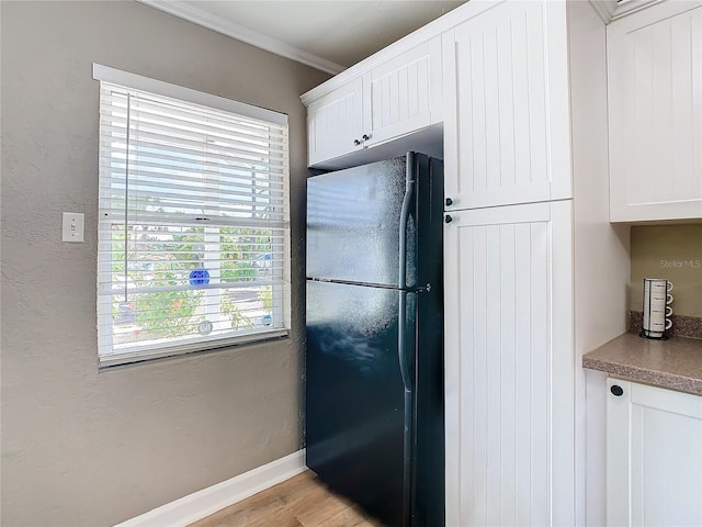 kitchen featuring ornamental molding, light hardwood / wood-style floors, white cabinetry, and black fridge