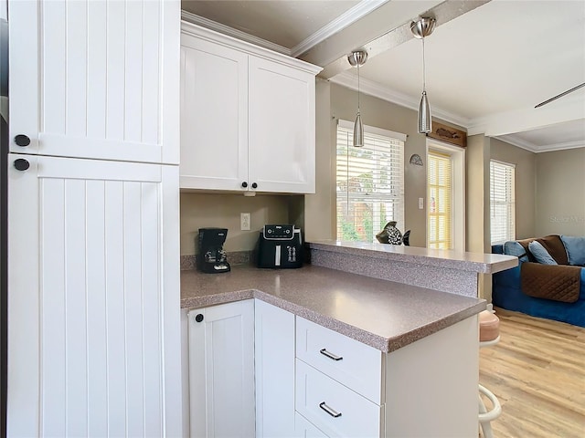 kitchen with white cabinets, kitchen peninsula, pendant lighting, wood-type flooring, and crown molding