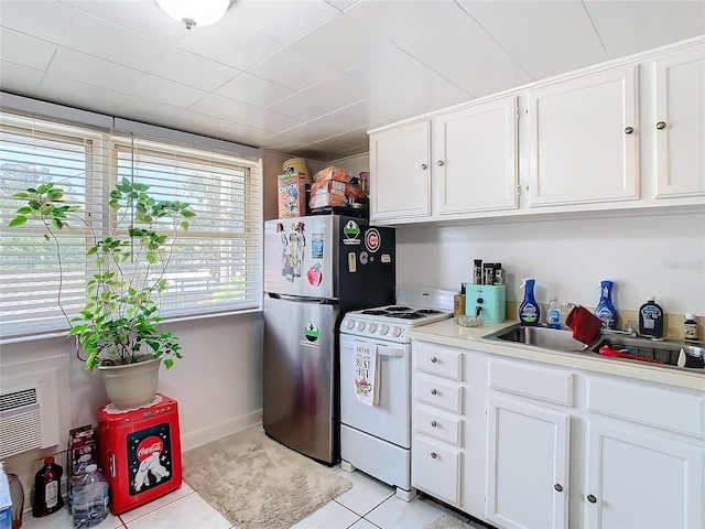 kitchen featuring white cabinets, sink, light tile patterned floors, stainless steel refrigerator, and white range oven