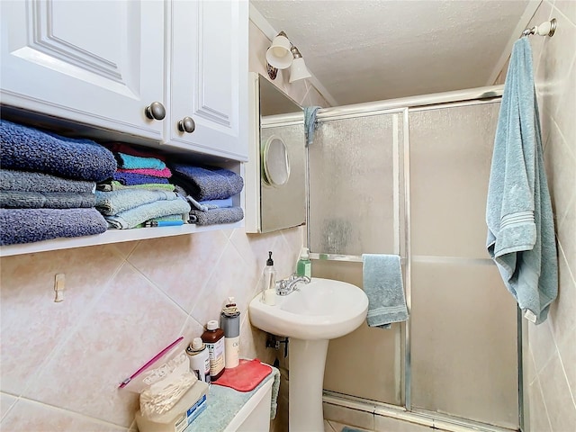 bathroom with a textured ceiling, tile walls, and a shower with shower door