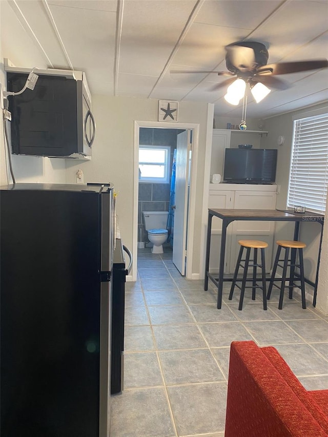 kitchen featuring a breakfast bar, white cabinetry, stainless steel appliances, light tile patterned floors, and ceiling fan