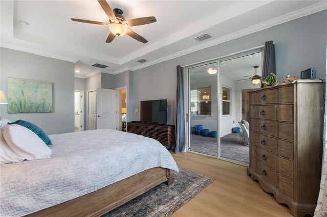 bedroom featuring light wood-type flooring, ornamental molding, a tray ceiling, and ceiling fan