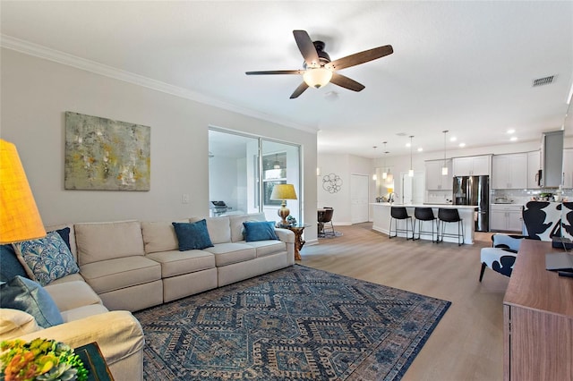 living room featuring ornamental molding, light hardwood / wood-style flooring, and ceiling fan