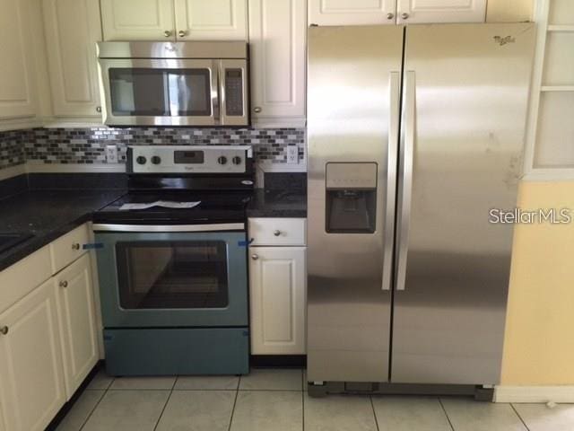 kitchen featuring decorative backsplash, white cabinetry, light tile patterned floors, and stainless steel appliances