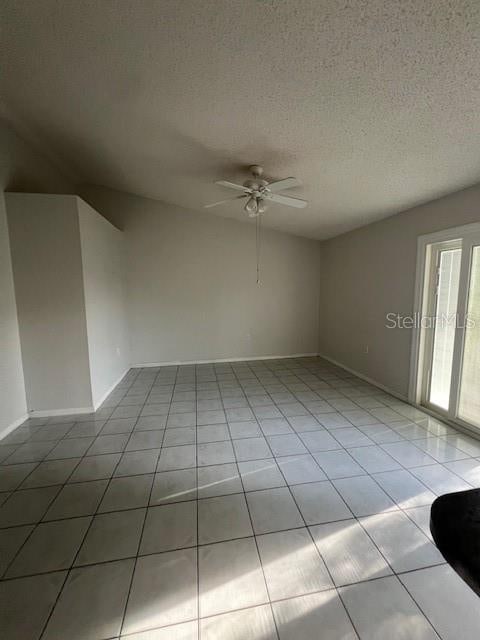 spare room featuring ceiling fan, light tile patterned floors, and a textured ceiling