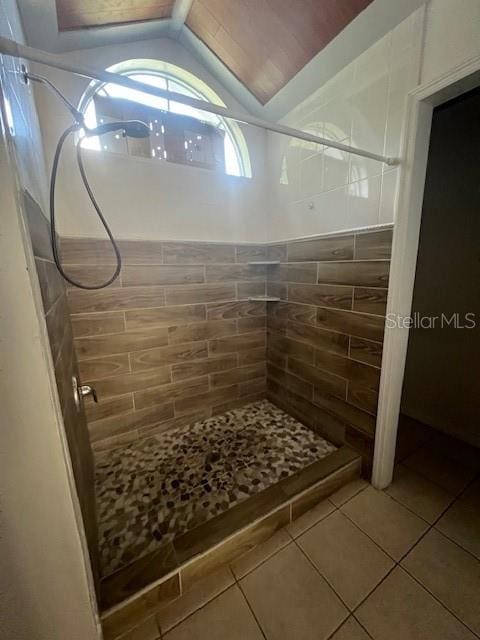 bathroom with a tile shower, tile walls, tile patterned flooring, and vaulted ceiling