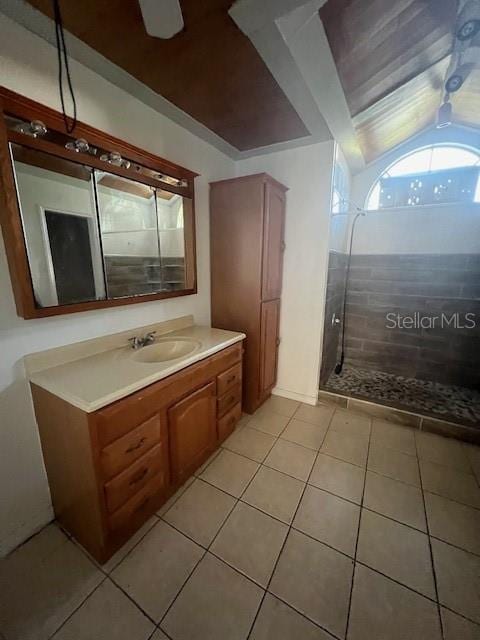 bathroom featuring tile patterned flooring, vanity, lofted ceiling, and tiled shower