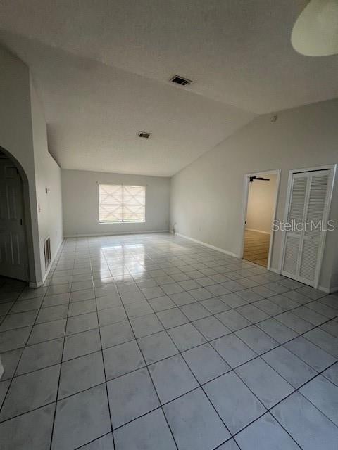 empty room featuring vaulted ceiling, ceiling fan, and light tile patterned flooring