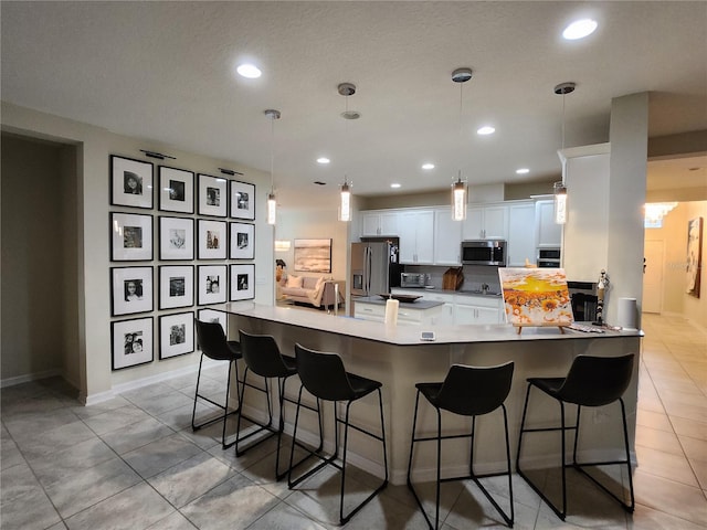 kitchen with hanging light fixtures, light tile patterned floors, white cabinetry, appliances with stainless steel finishes, and a breakfast bar area