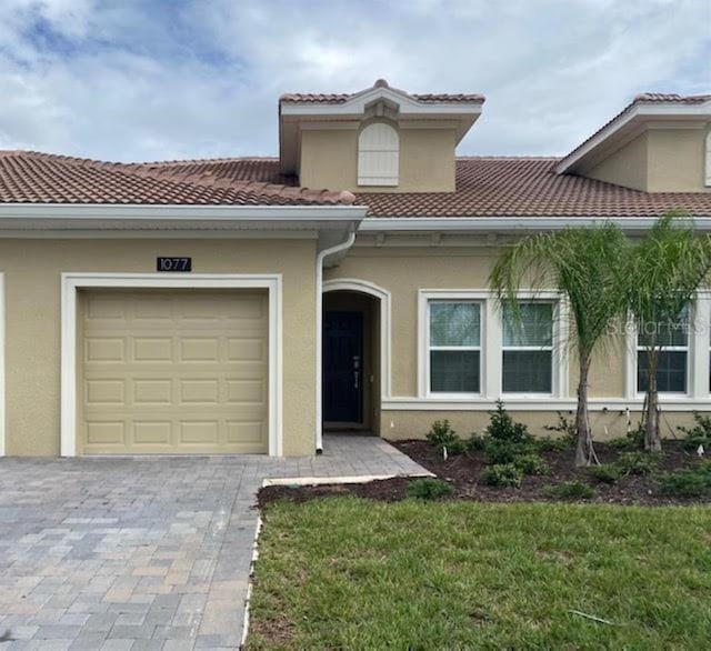 view of front of house with decorative driveway, a tile roof, an attached garage, and stucco siding