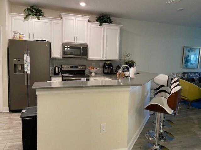 kitchen with a breakfast bar, light wood-type flooring, white cabinetry, decorative backsplash, and stainless steel appliances