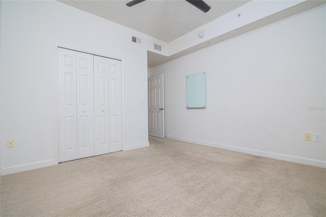 unfurnished bedroom with ceiling fan, a textured ceiling, a closet, and light carpet