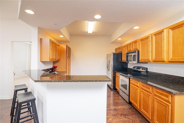 4177 N Orange Blossom Trl Unit 210, Orlando, FL 32804 - kitchen with stainless steel appliances, a textured ceiling, a peninsula, a kitchen bar, and dark wood-type flooring
