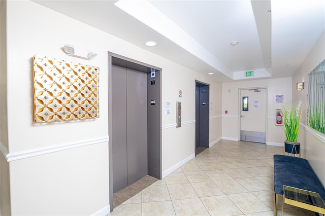 hallway featuring a raised ceiling, elevator, and light tile patterned floors